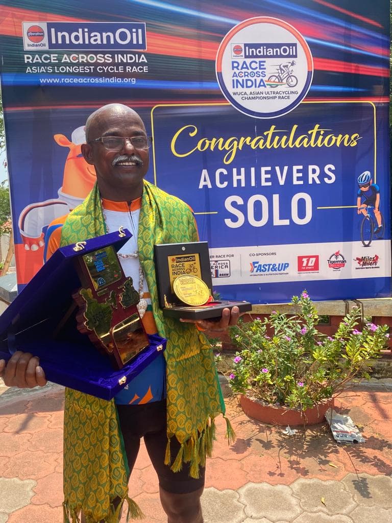 Bobba Ravinder Reddy holding his trophy and medal in front of the IndianOil Race Across India 'Congratulations Achievers Solo' banner
