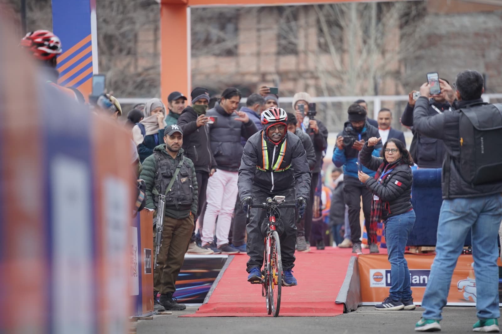 Bobba Ravinder Reddy cycling down the red carpet at an IndianOil Race Across India finish area, crowd photographing him