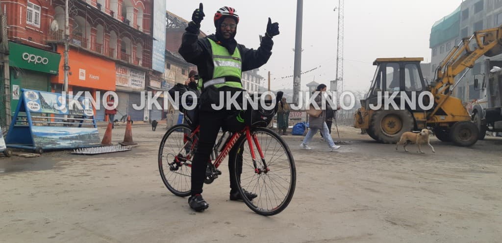 Bobba Ravinder Reddy giving a thumbs up on a Kashmir street with a JCB excavator and a dog in the background