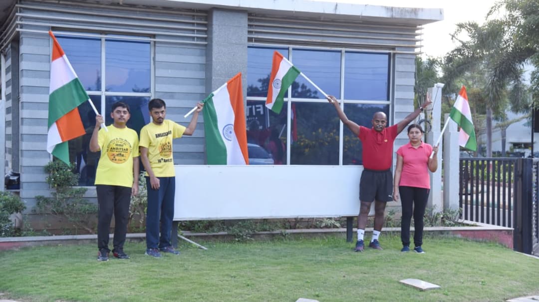 Family holding Indian flags outside their home, two wearing yellow Amritsar Half Marathon Ambassador T-shirts