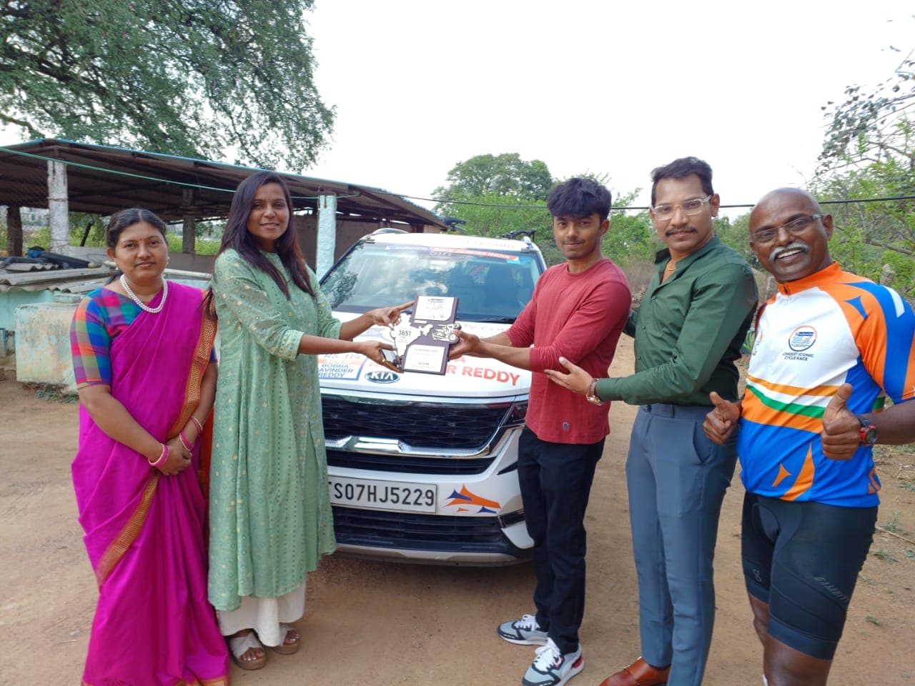 Family members and Bobba Ravinder Reddy posing with commemorative plaques beside the branded support car