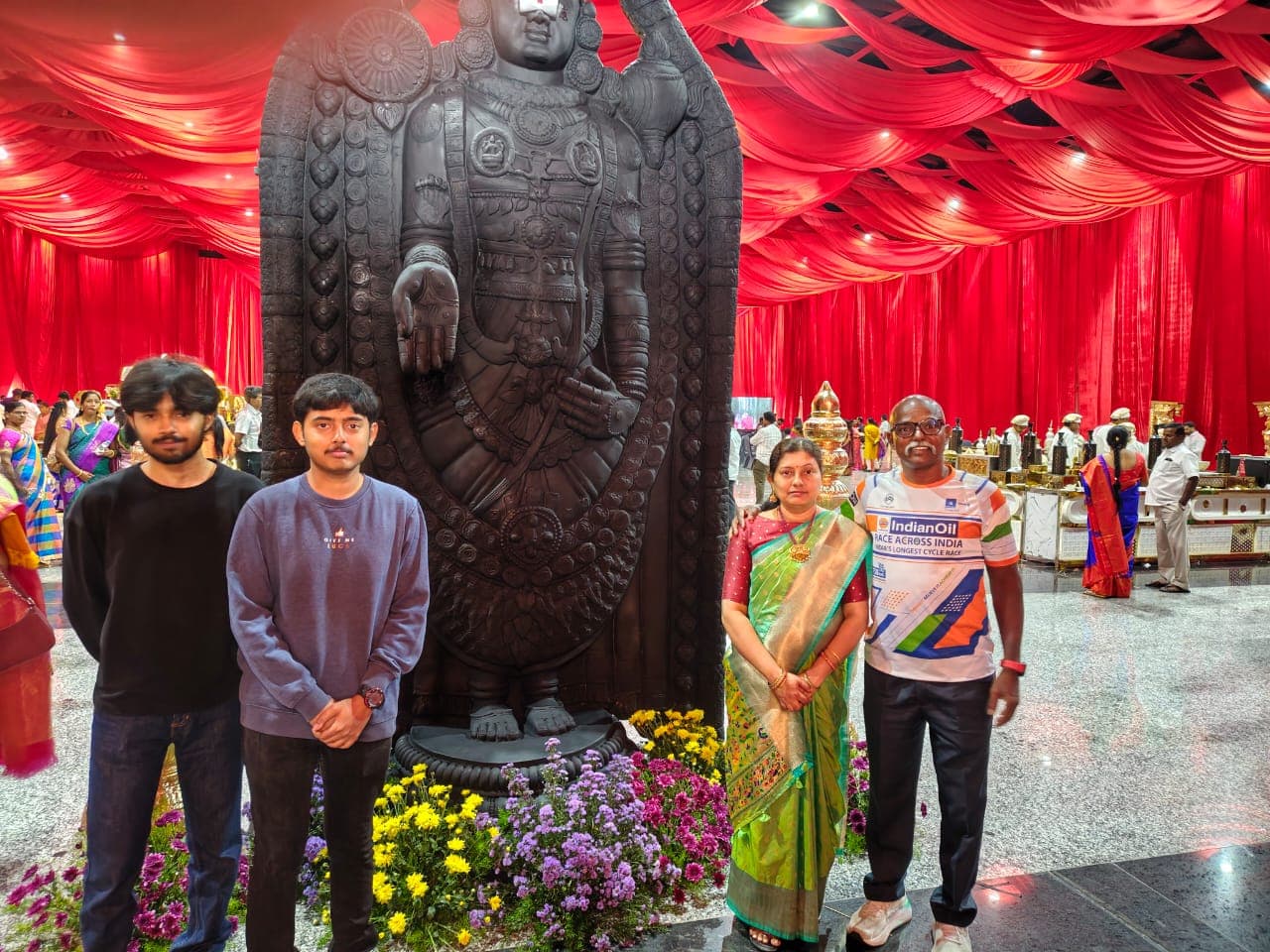 Family posing in front of a large Lord Venkateswara statue at a festive red-draped venue