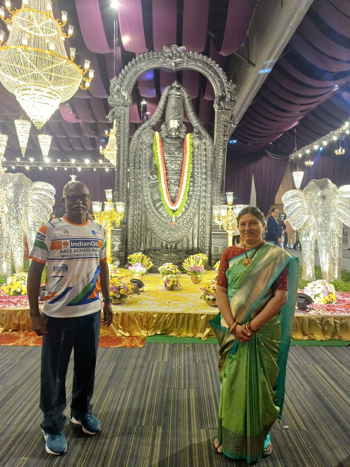 Bobba Ravinder Reddy and his wife posing before a silver Lord Venkateswara idol at a decorated event hall