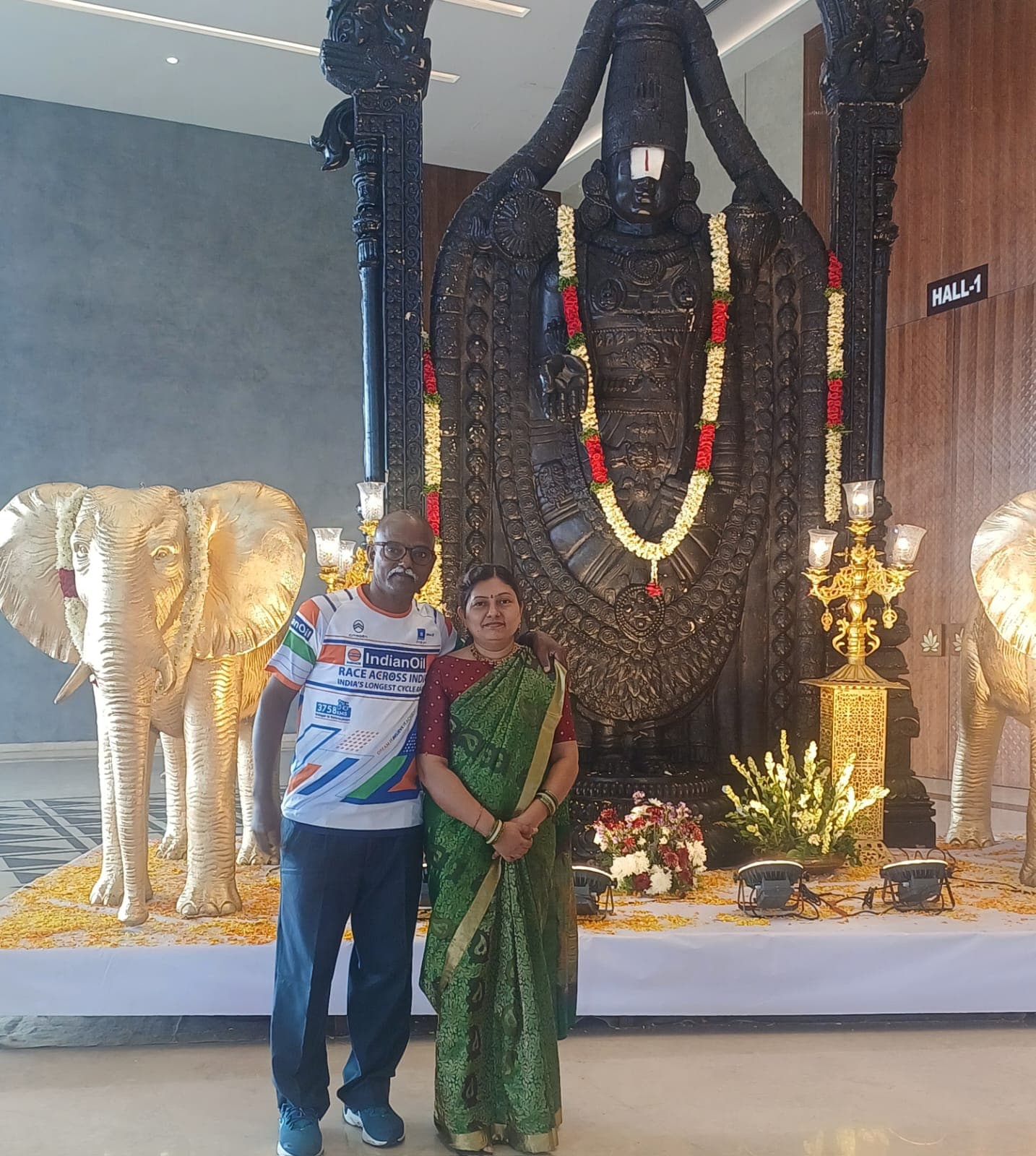 Bobba Ravinder Reddy and his wife in front of a black Lord Venkateswara statue flanked by golden elephant sculptures