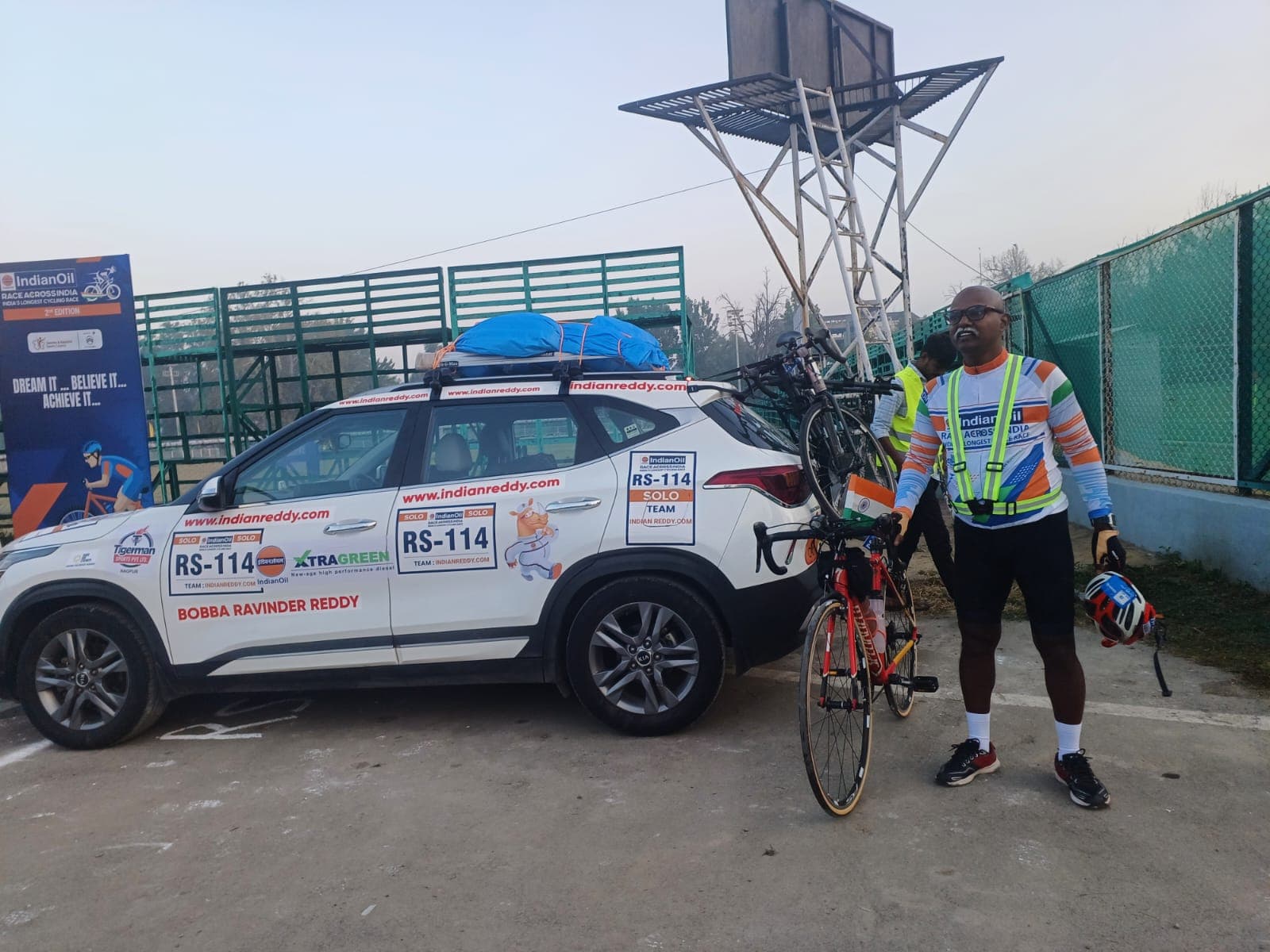 Bobba Ravinder Reddy standing beside his RS-114 branded support car and bicycle before the IndianOil Race Across India, 2nd edition