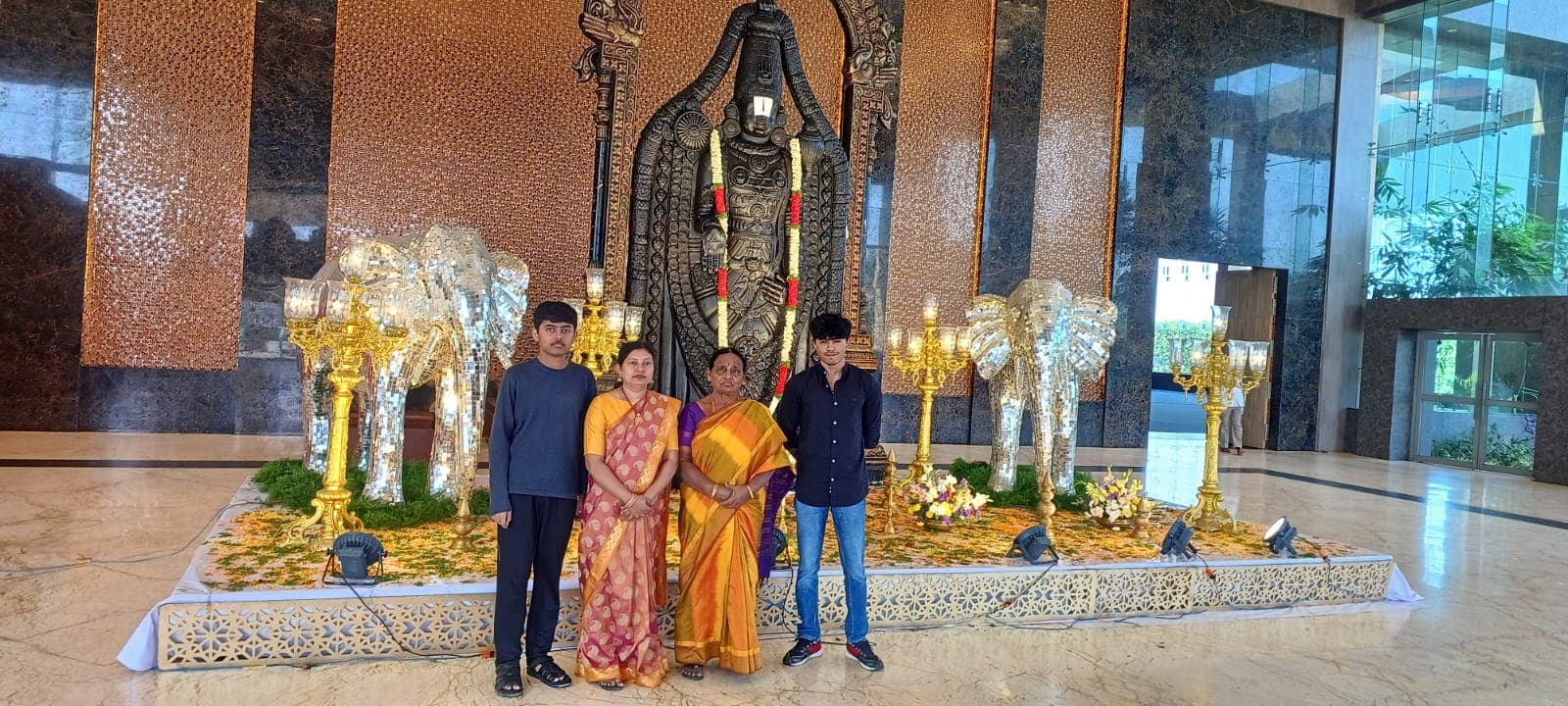 Two sons with their mother and grandmother in front of a black Lord Venkateswara statue flanked by silver elephant sculptures