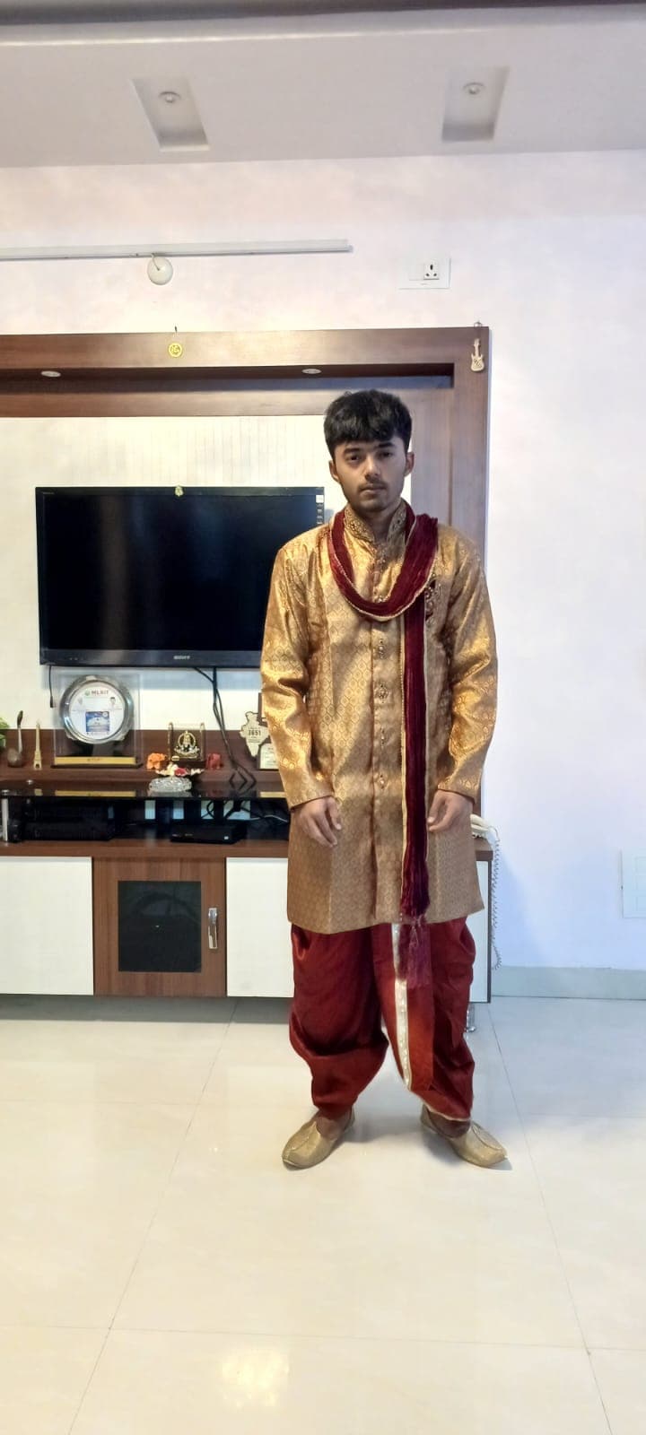 One of the sons dressed in a traditional gold sherwani and dhoti at home