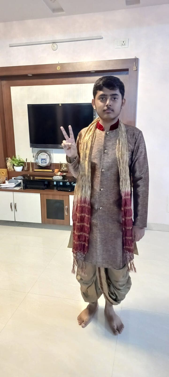 The other son in traditional attire giving a peace sign at home