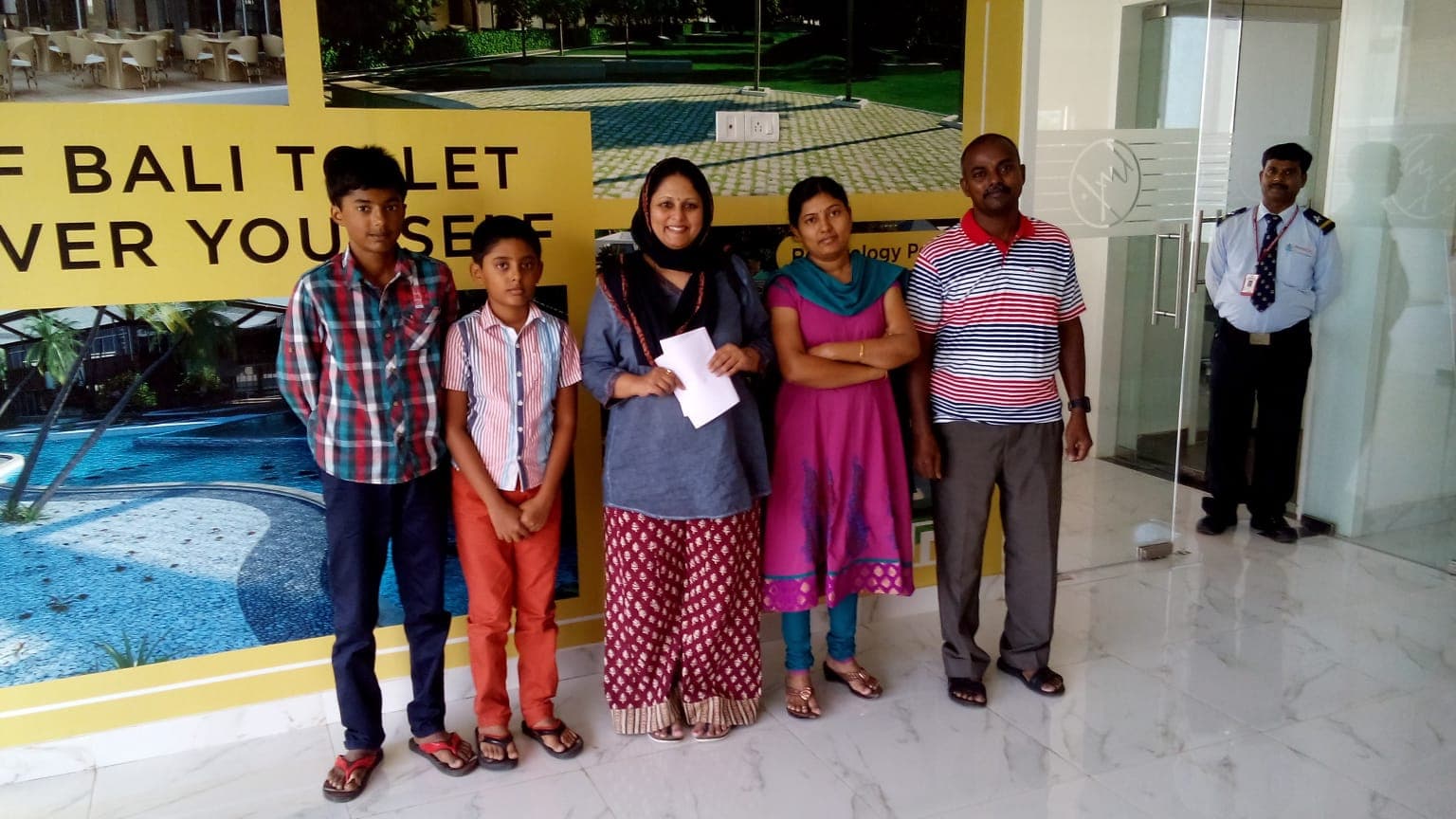 Family group photo in a building lobby beside a resort-themed advertisement poster