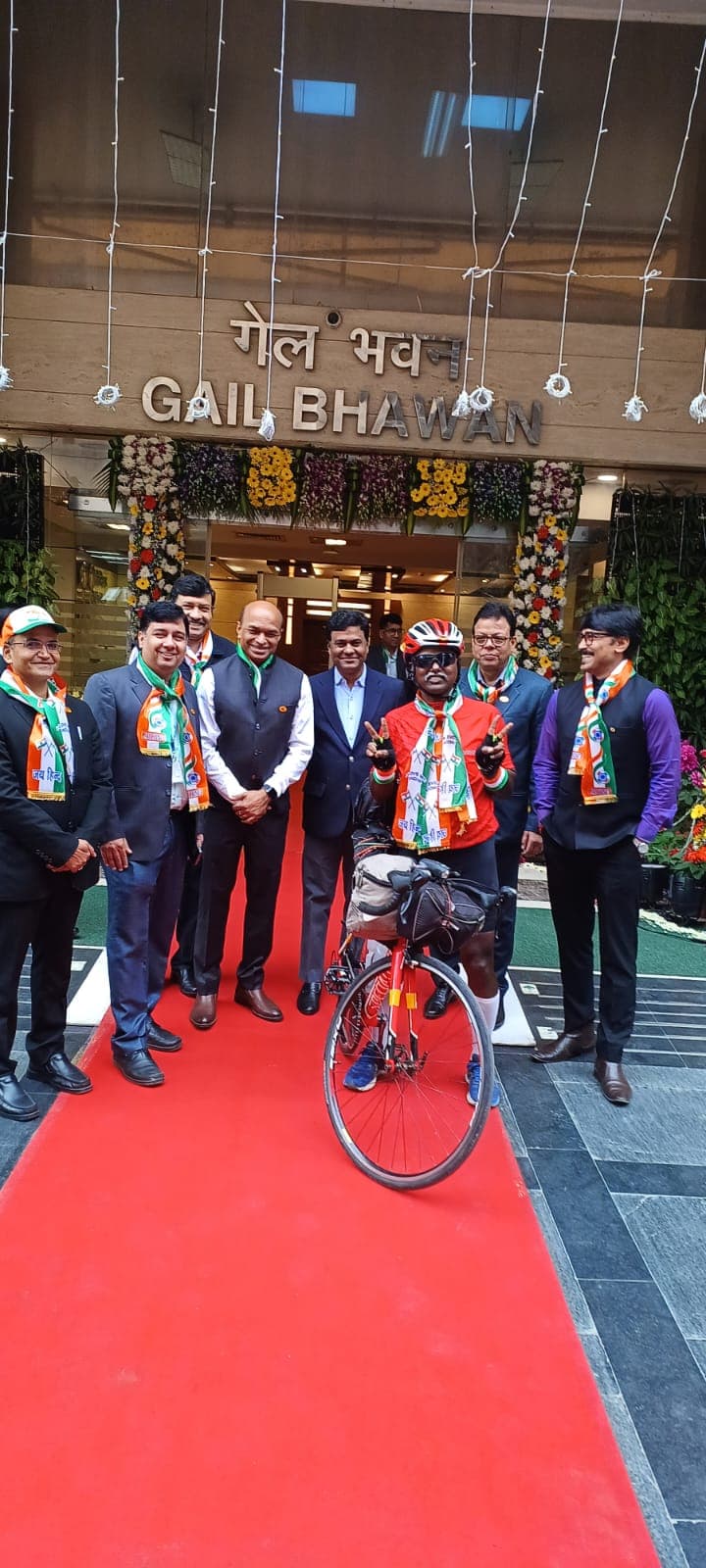 Bobba Ravinder Reddy posing with his bicycle in front of the GAIL Bhawan entrance decorated with flowers and streamers