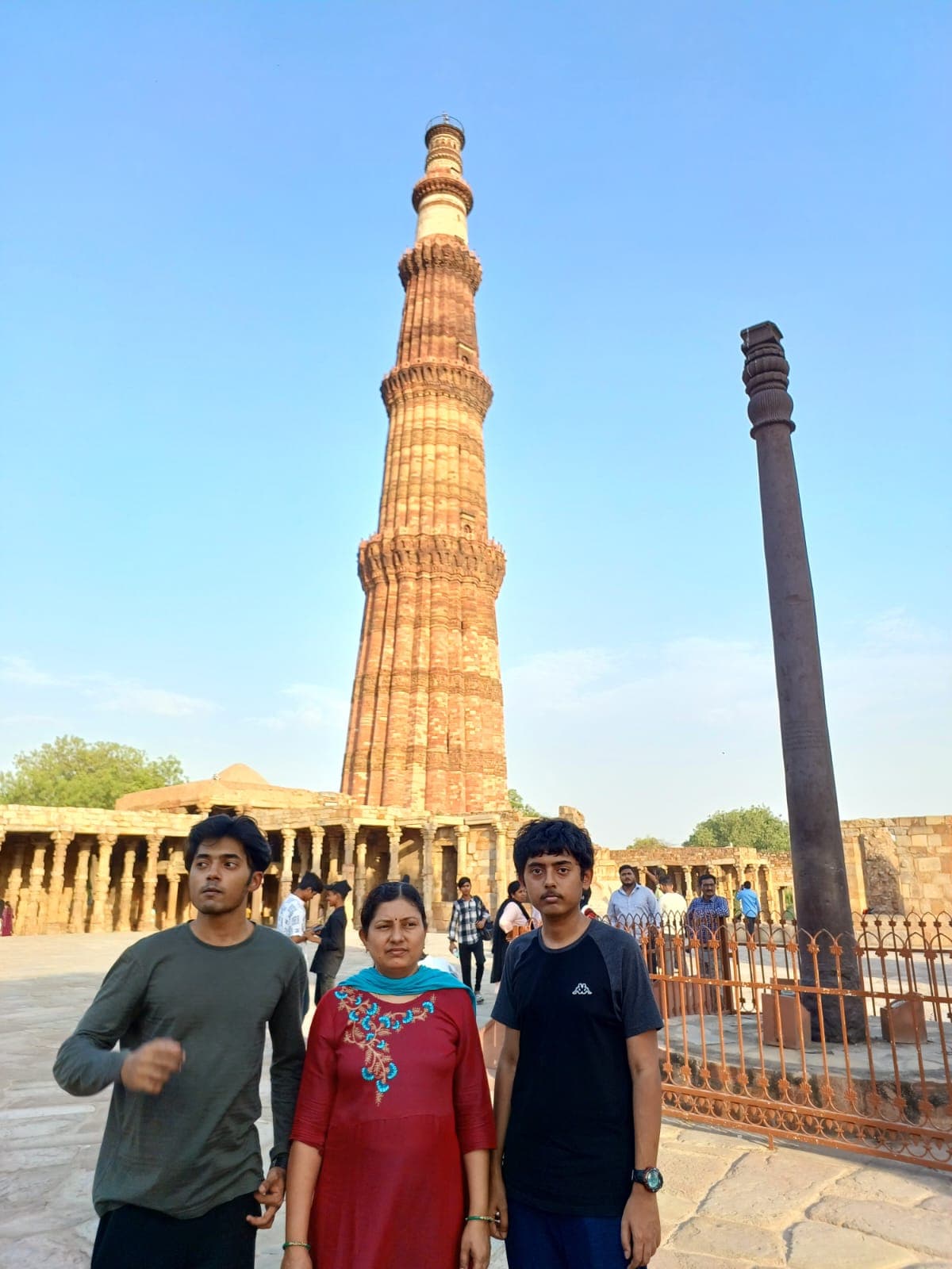 Two sons and their mother posing with the Qutub Minar towering behind them