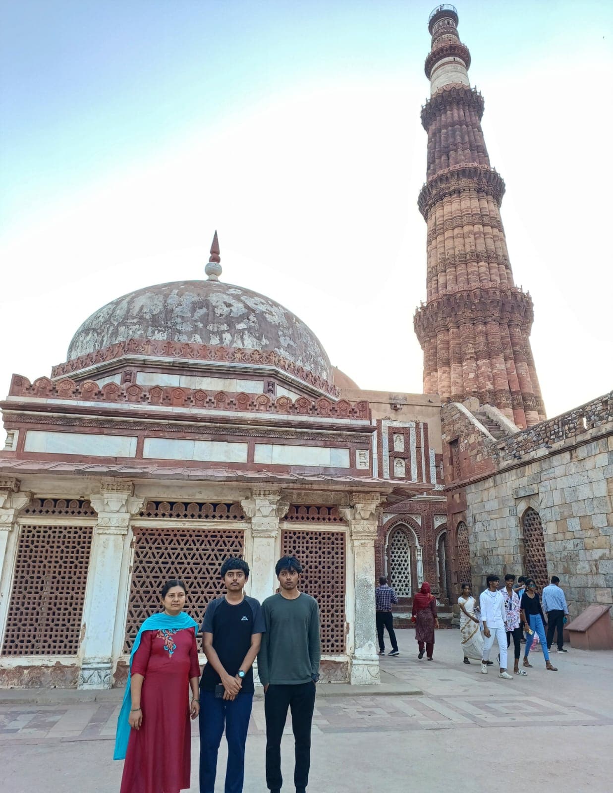 Two sons and their mother beside a domed tomb structure in the Qutub Minar complex