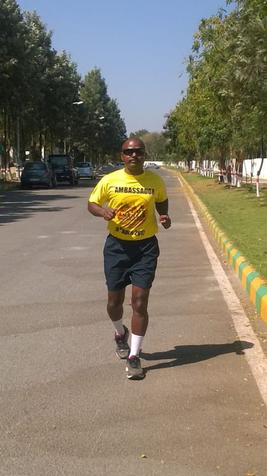 Bobba Ravinder Reddy running on a tree-lined road wearing an Ambassador shirt